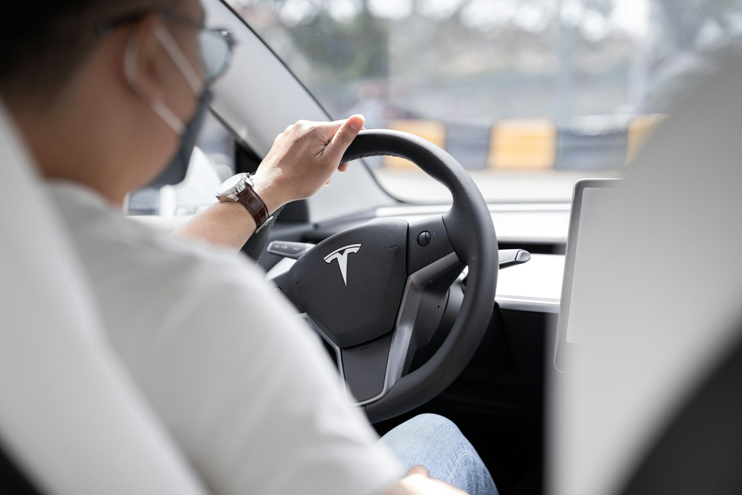 Close-up photo of a person driving a Tesla, showcasing modern vehicle interior design.